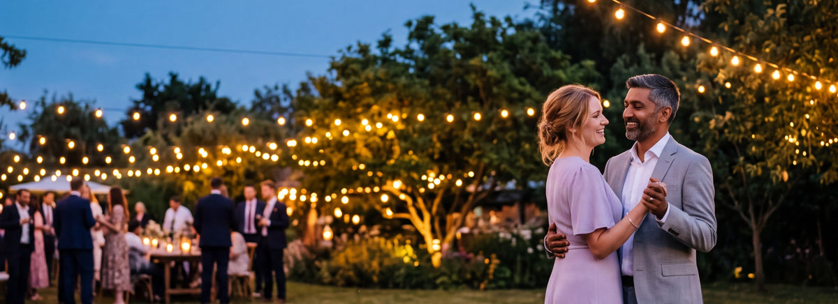 A couple slow dancing close together at an evening garden party under string lights