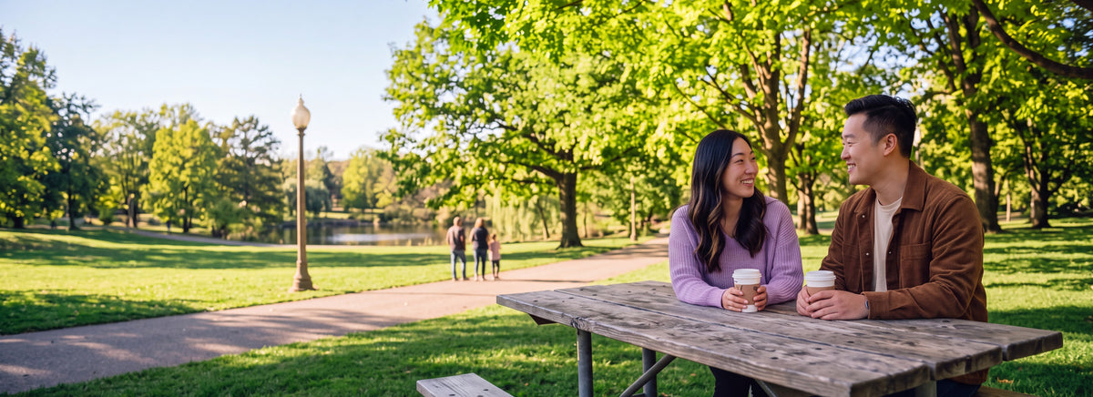 A couple sharing coffee at a picnic table in a green park