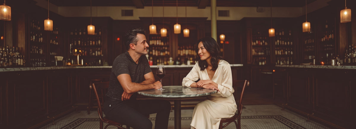 A couple talking across a small marble table in a warmly lit wine bar