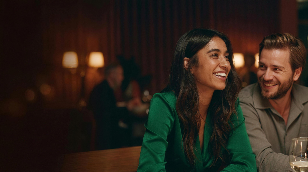 A woman laughing with her partner over dinner in a warmly lit restaurant